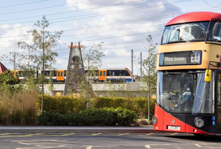 A red double-decker bus is parked near a train track with a train passing by.