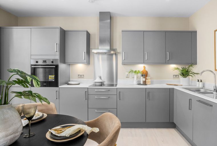 A modern kitchen with grey cabinets, a stainless steel range hood, and a dining table.