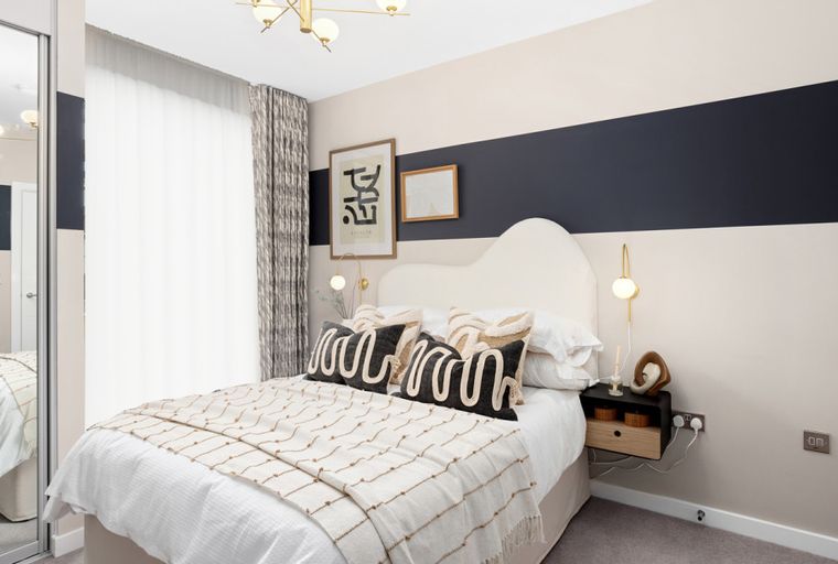 A bedroom with a bed, pillows, a nightstand, and a wall lamp.