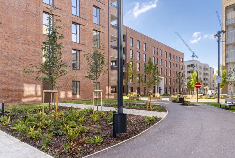 A modern residential complex with brick buildings, landscaped gardens, and paved walkways.