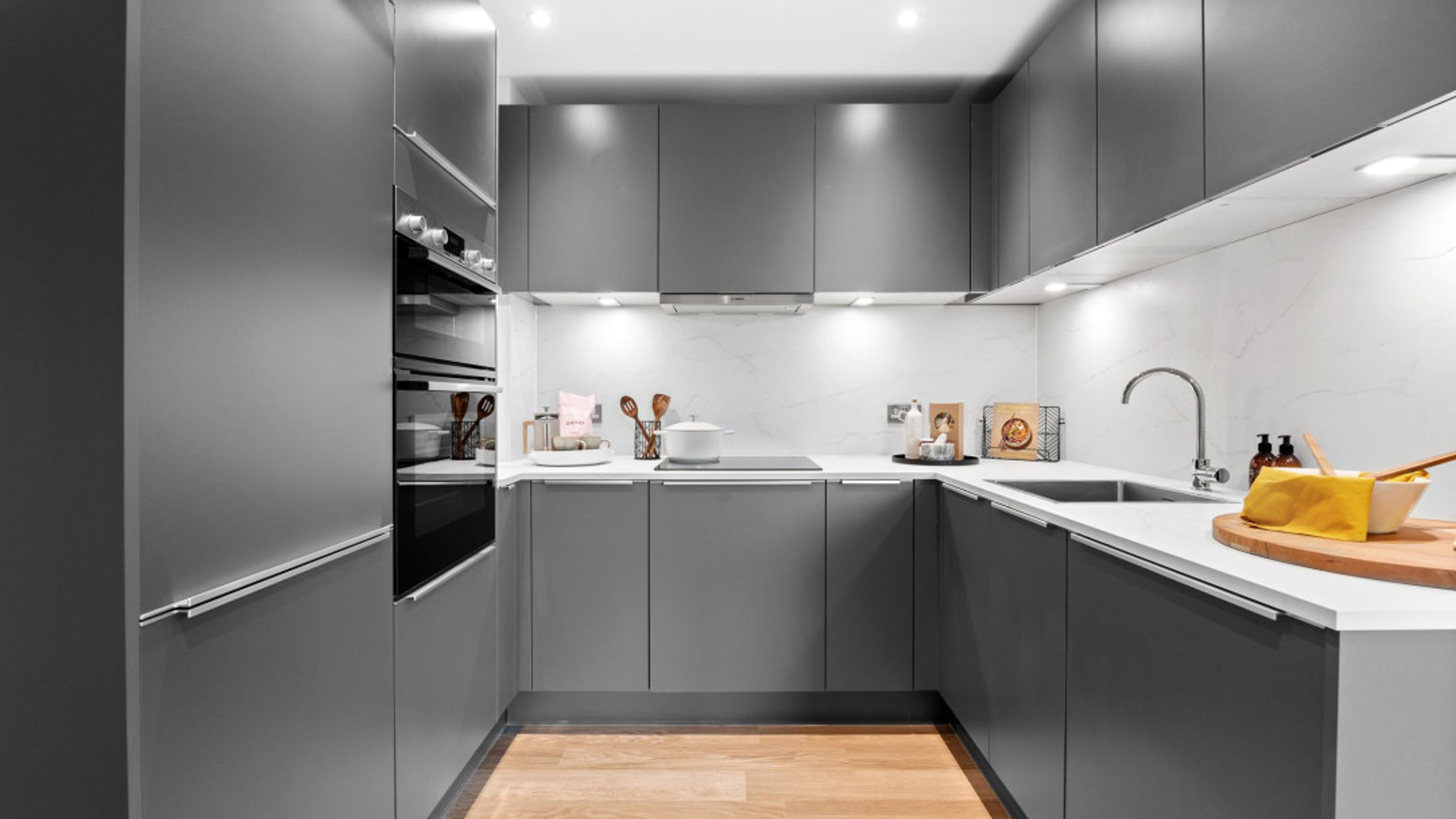 A modern U-shaped kitchen with grey cabinets, integrated ovens, a sink, and a stovetop.
