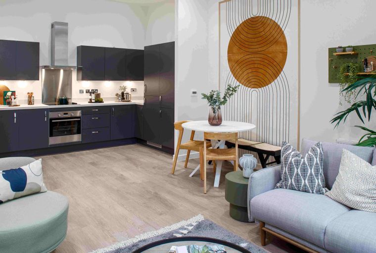 A modern open-plan living area and kitchen with a dining table, sofa, and kitchen cabinets.