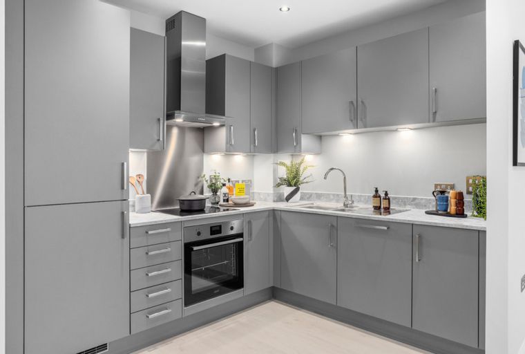 A modern L-shaped kitchen with grey cabinets, a stainless steel backsplash, and an integrated oven.