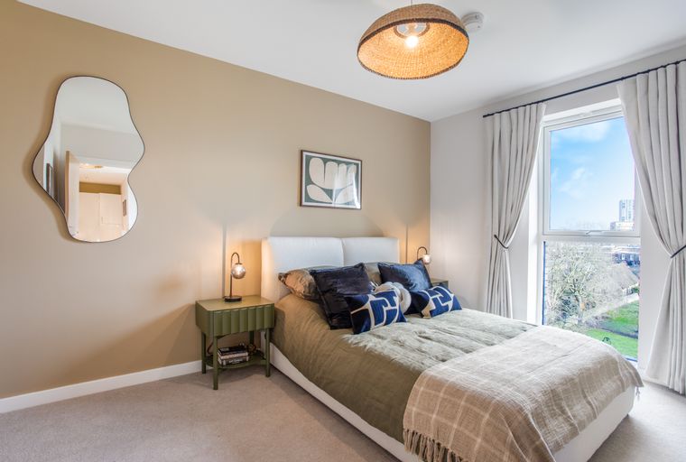 A bedroom with a bed, pillows, a nightstand, a lamp, a mirror, and a window.