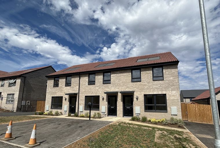 A row of modern townhouses with brick exteriors and dark windows under a cloudy blue sky.
