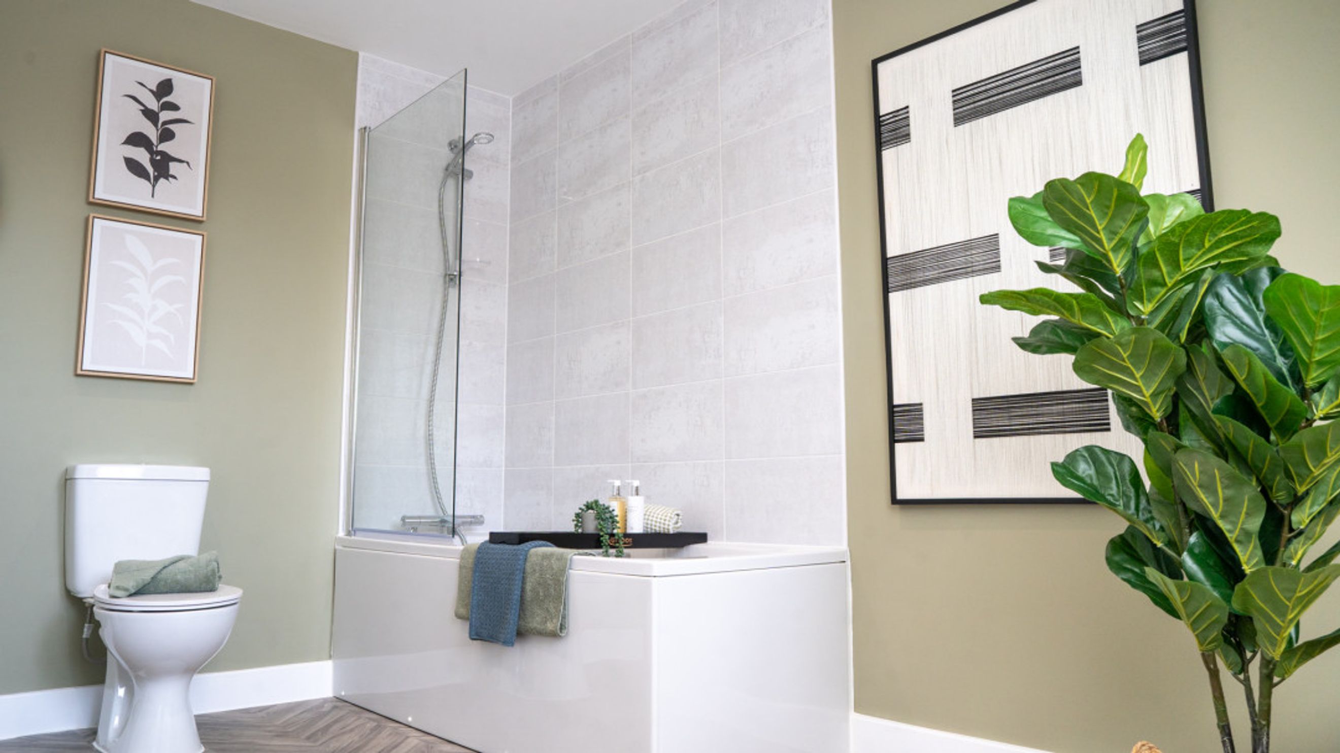 A bathroom with a toilet, bathtub, shower screen, and artwork.
