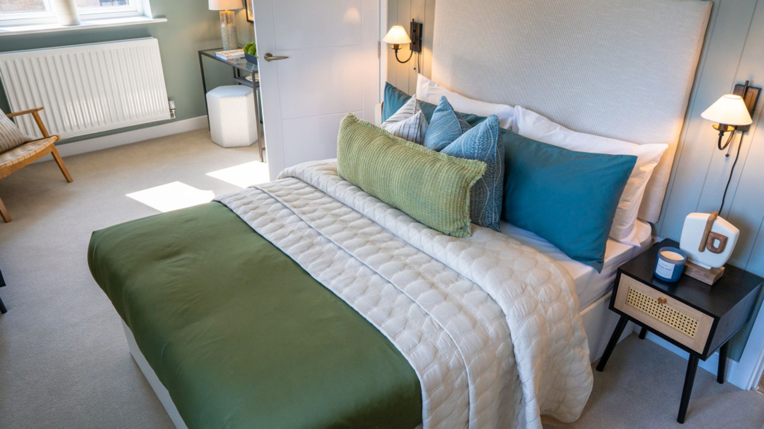 A bedroom with a bed, pillows, a quilted throw, a bedside table, and a chair.