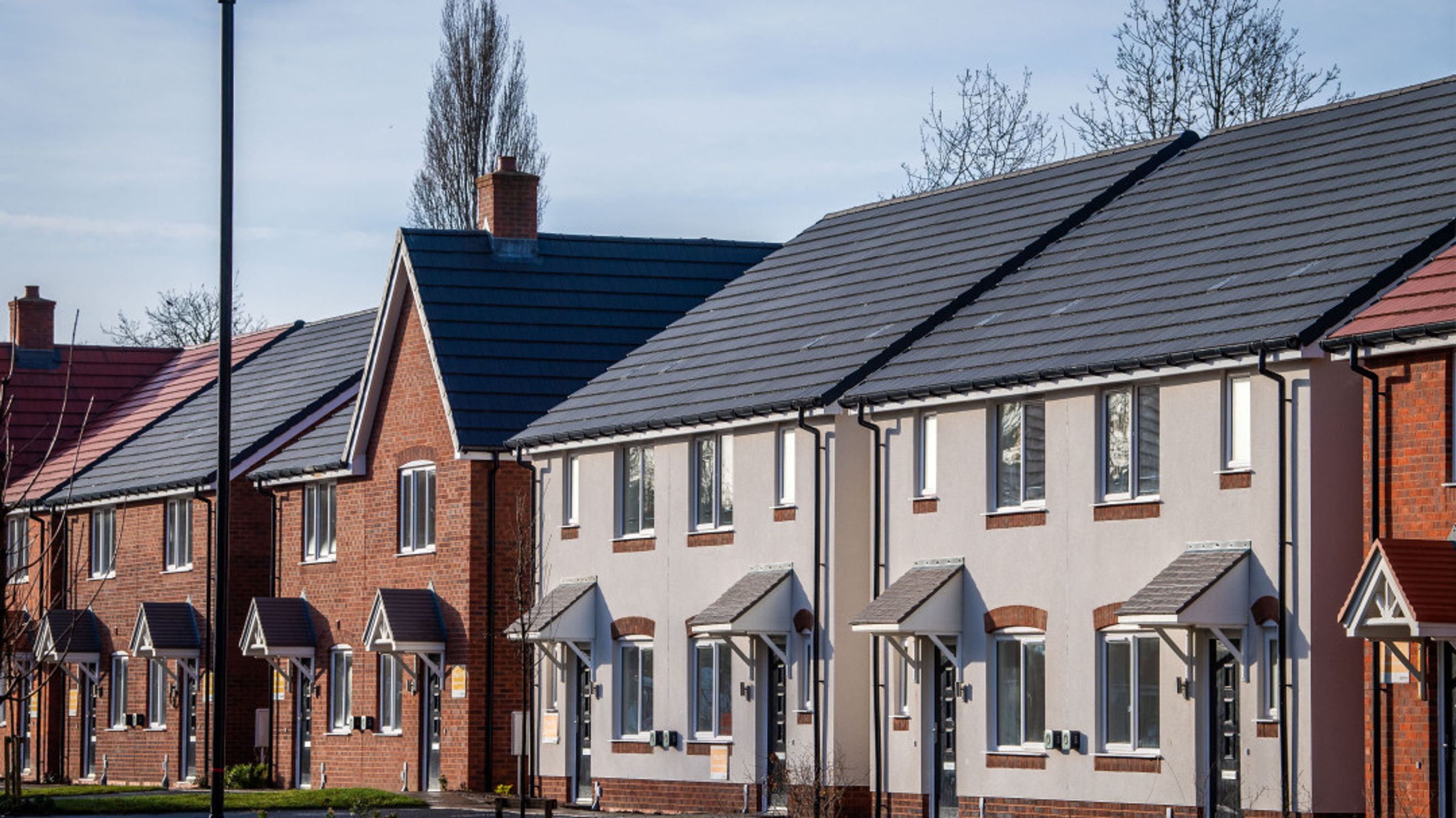 A row of modern houses with brick and stucco exteriors and dark tiled roofs.