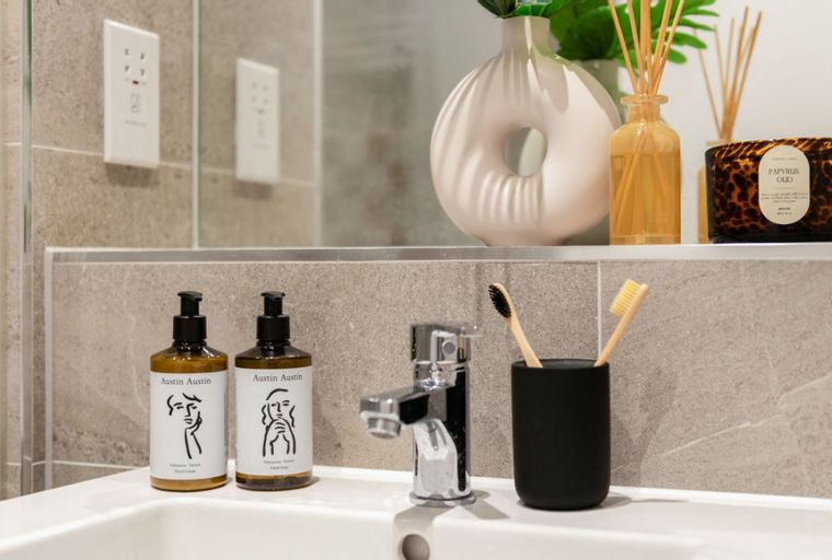 A bathroom sink with a chrome faucet, two bottles of hand soap, and a toothbrush holder with two toothbrushes.