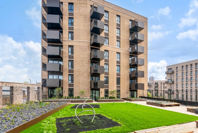 A modern apartment building with balconies overlooking a communal garden with grass and seating areas.