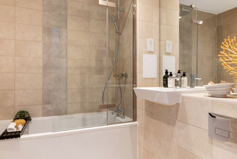 A bathroom with a bathtub, shower, sink, and tiled walls.