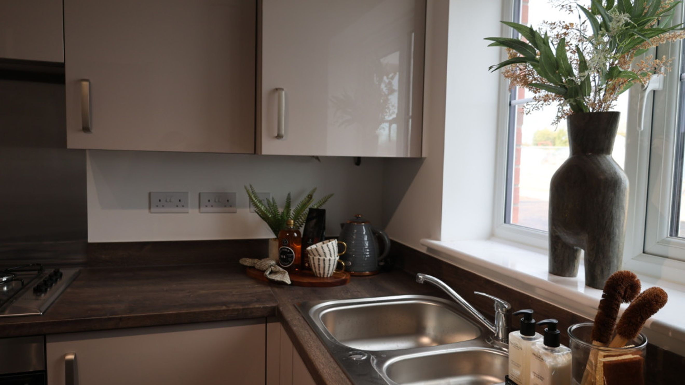 A kitchen counter with a double sink, kettle, and decorative items.
