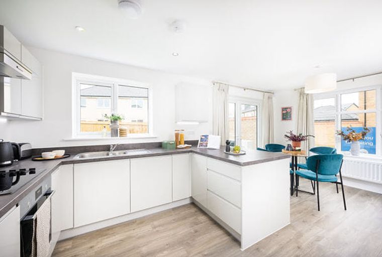 A modern kitchen with white cabinets, a sink, and a dining area with teal chairs.
