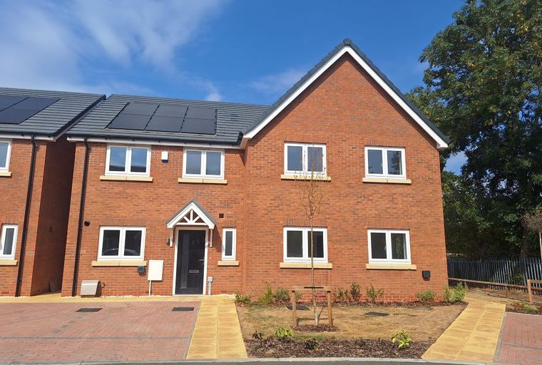 A modern red brick house with white-framed windows and a grey roof with solar panels.
