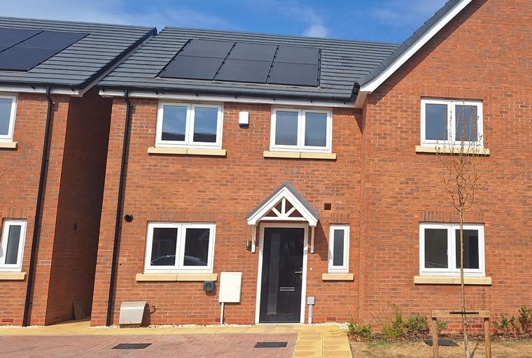A brick house with solar panels on the roof and white-framed windows.