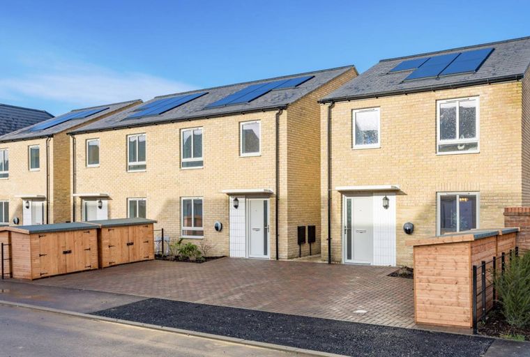 A row of modern townhouses with light yellow brick exteriors and solar panels on the roof.
