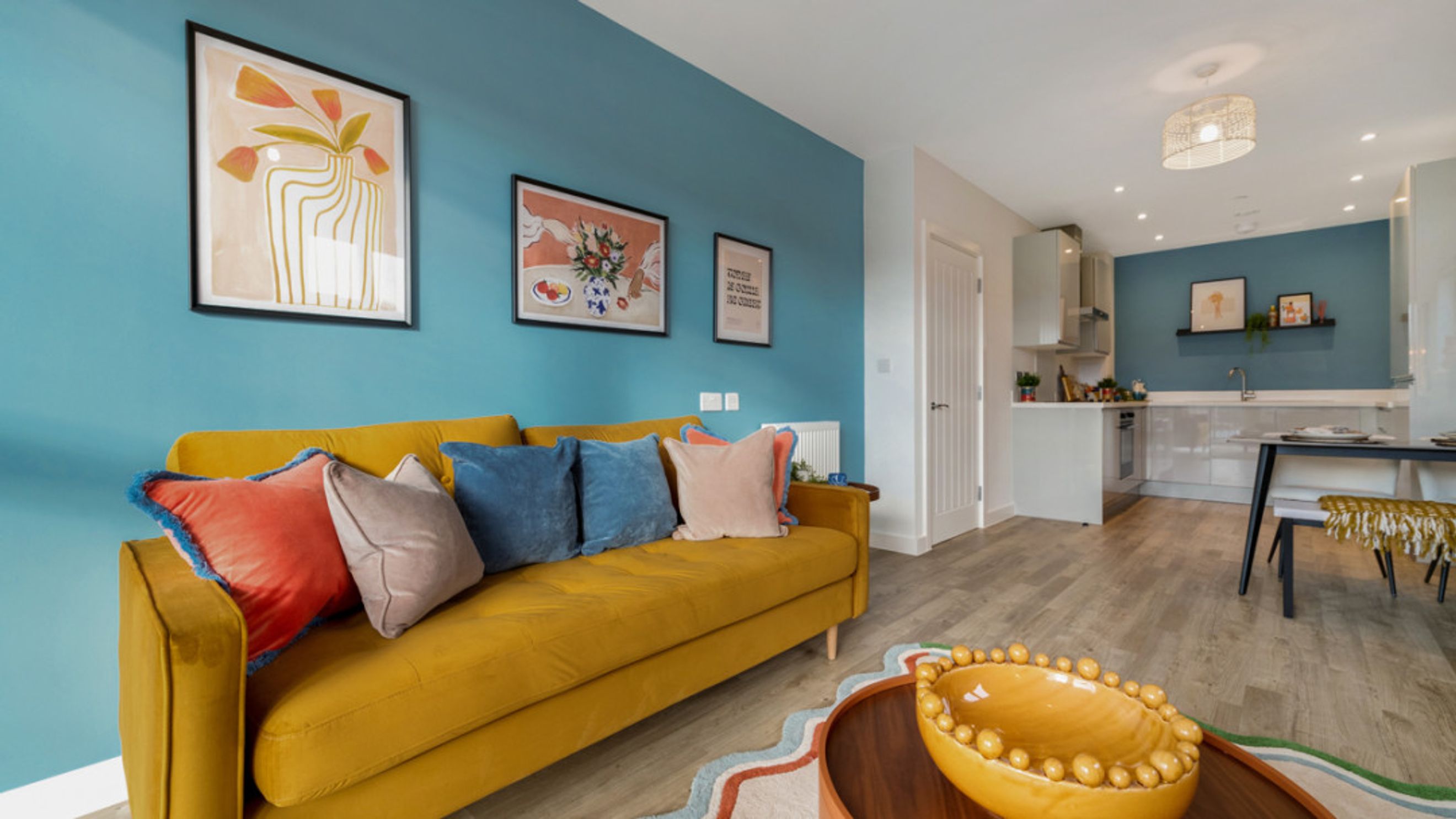 A living room and kitchen area with a yellow sofa, artwork, and a kitchen island.