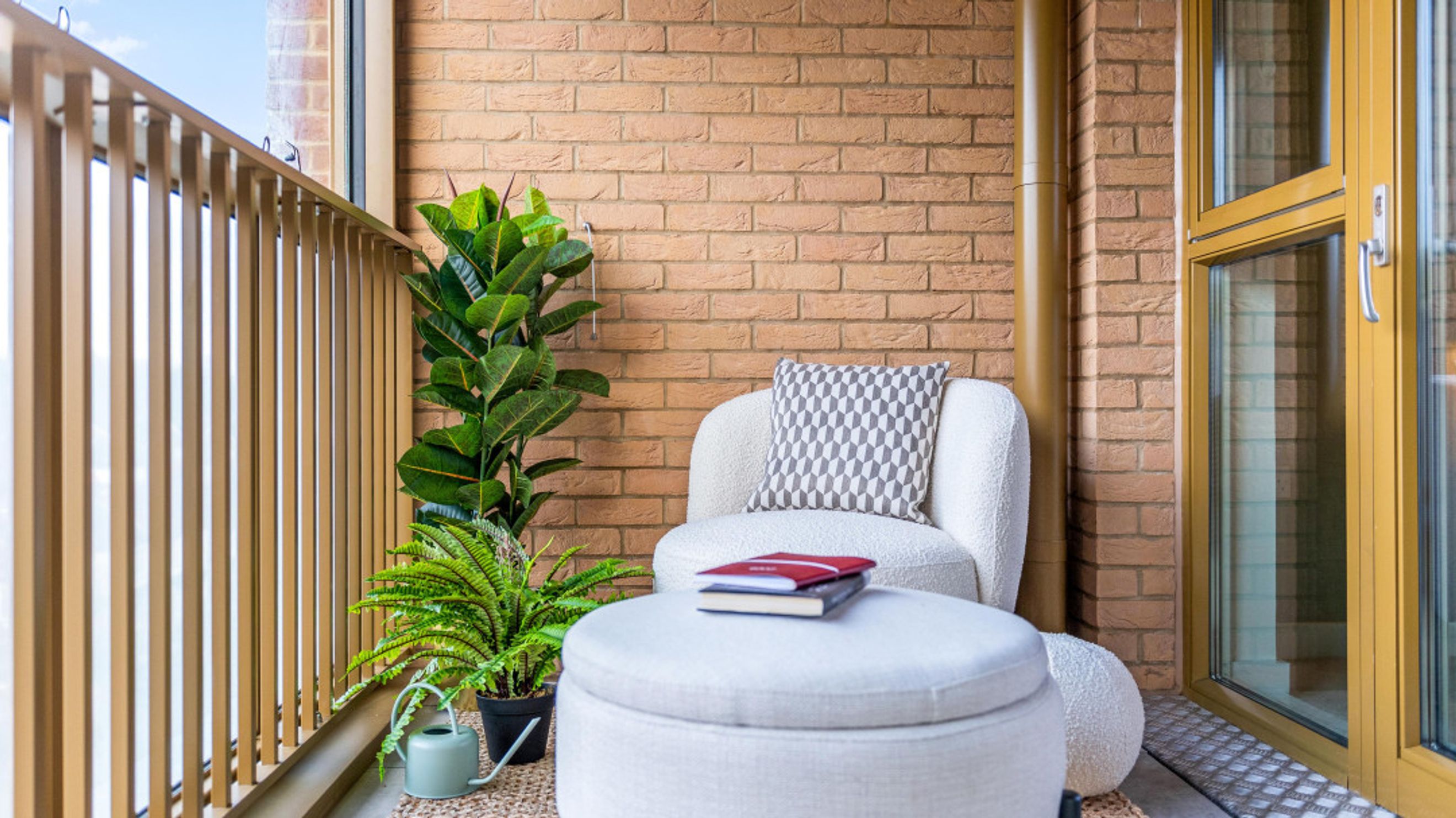 A balcony with a chair, ottoman, plants, and a watering can.