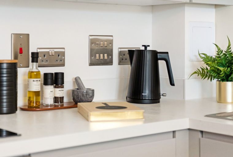 A kitchen countertop with a black kettle, spices, and electrical outlets.