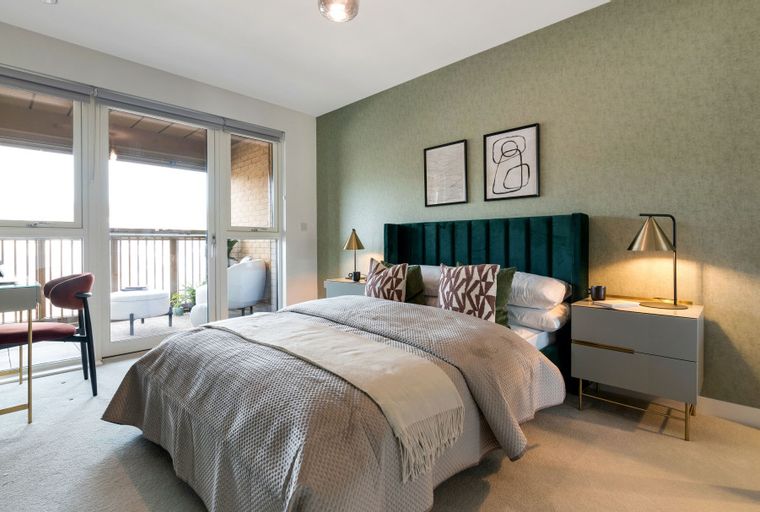 A bedroom with a bed, bedside tables, a desk, and balcony doors.