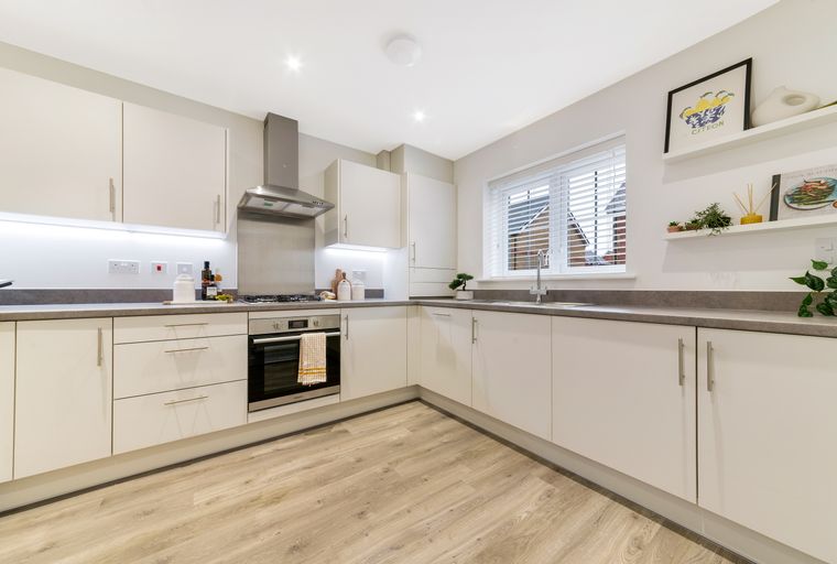 A modern kitchen with cream cabinets, a grey countertop, and a stainless steel oven.