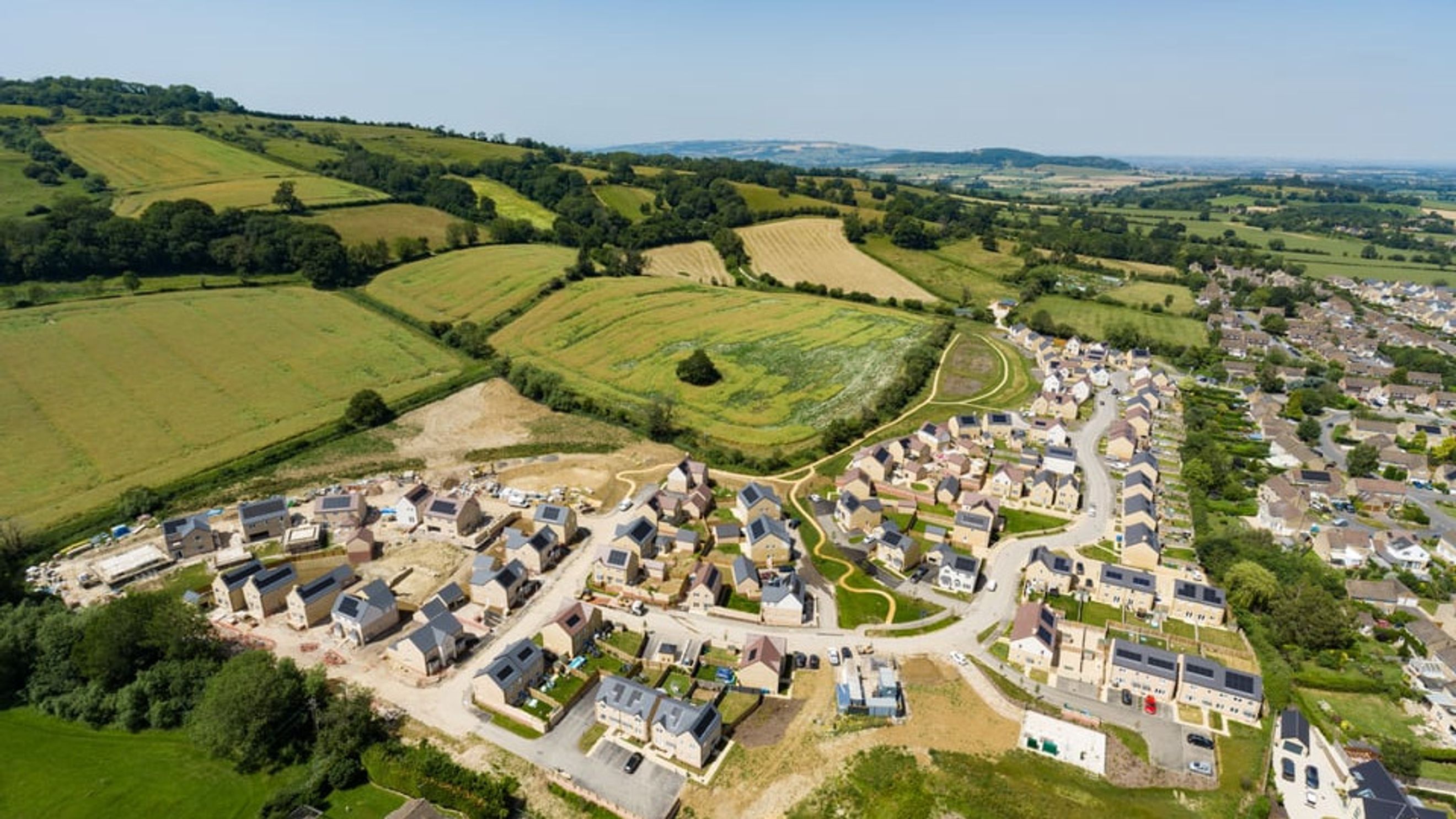 An aerial view of a new housing development surrounded by green fields and hills.