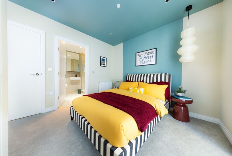 A bedroom with a bed, pillows, and a sign on the wall.