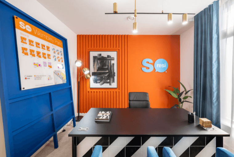 A modern office space with a black desk, orange wall, and a large display board.