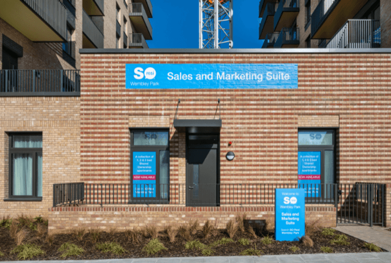 A sales and marketing suite for SO Resi Wembley Park with a sign and windows displaying apartment information.