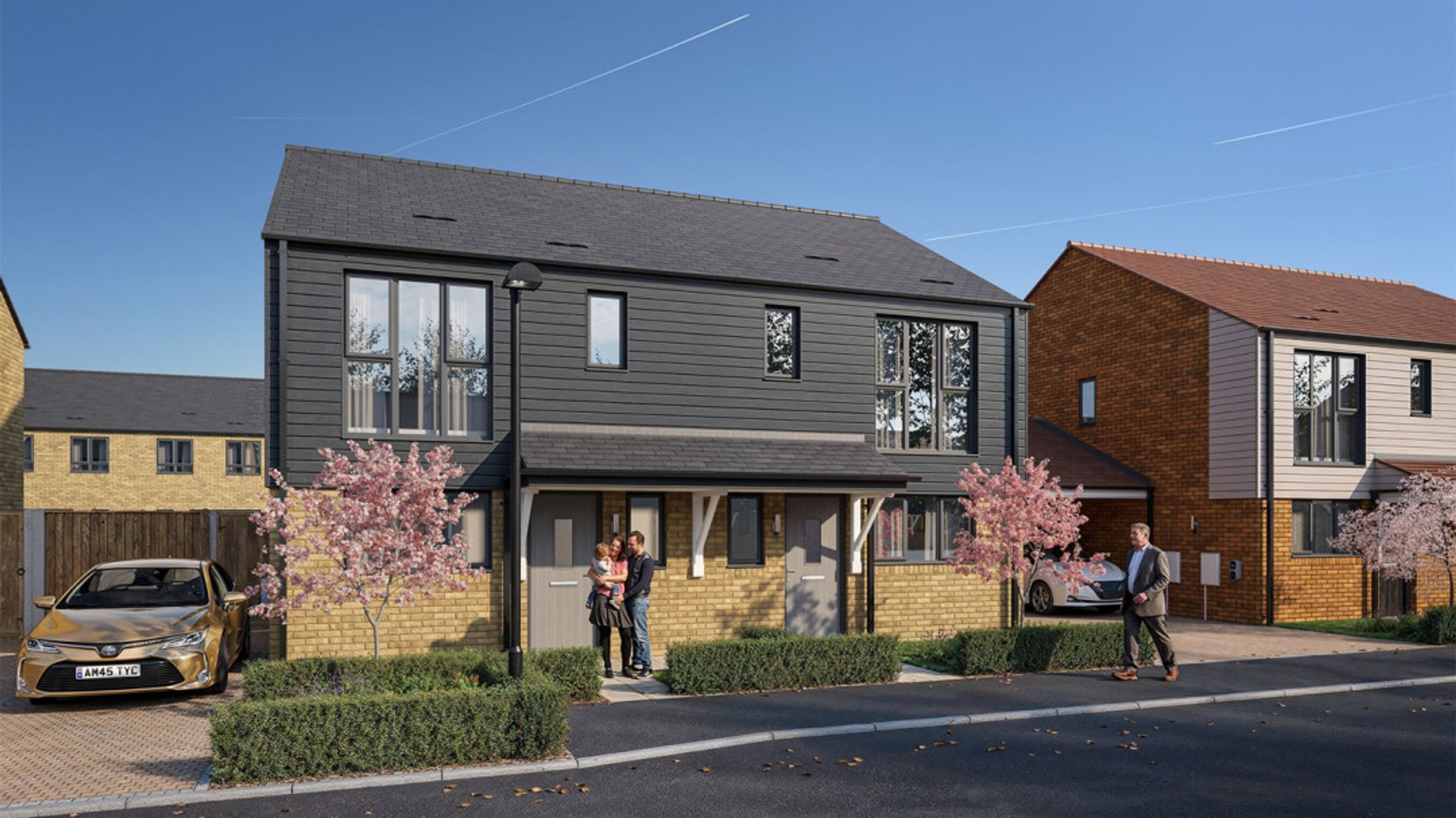 A row of modern houses with dark cladding and brick exteriors, featuring trees and a car.