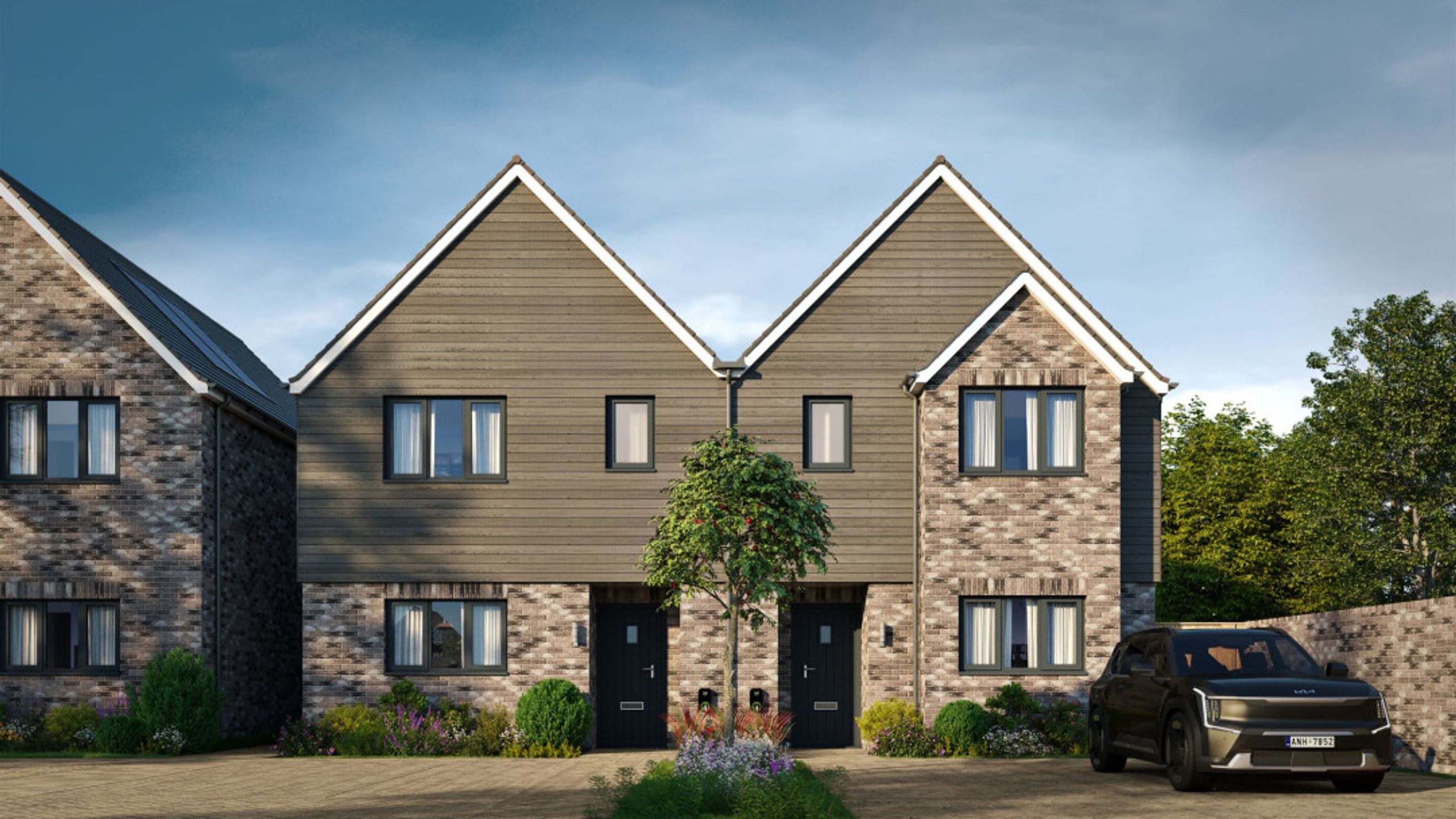 A row of modern townhouses with brick and wood exteriors, featuring multiple windows and front doors, with a car parked in the driveway.