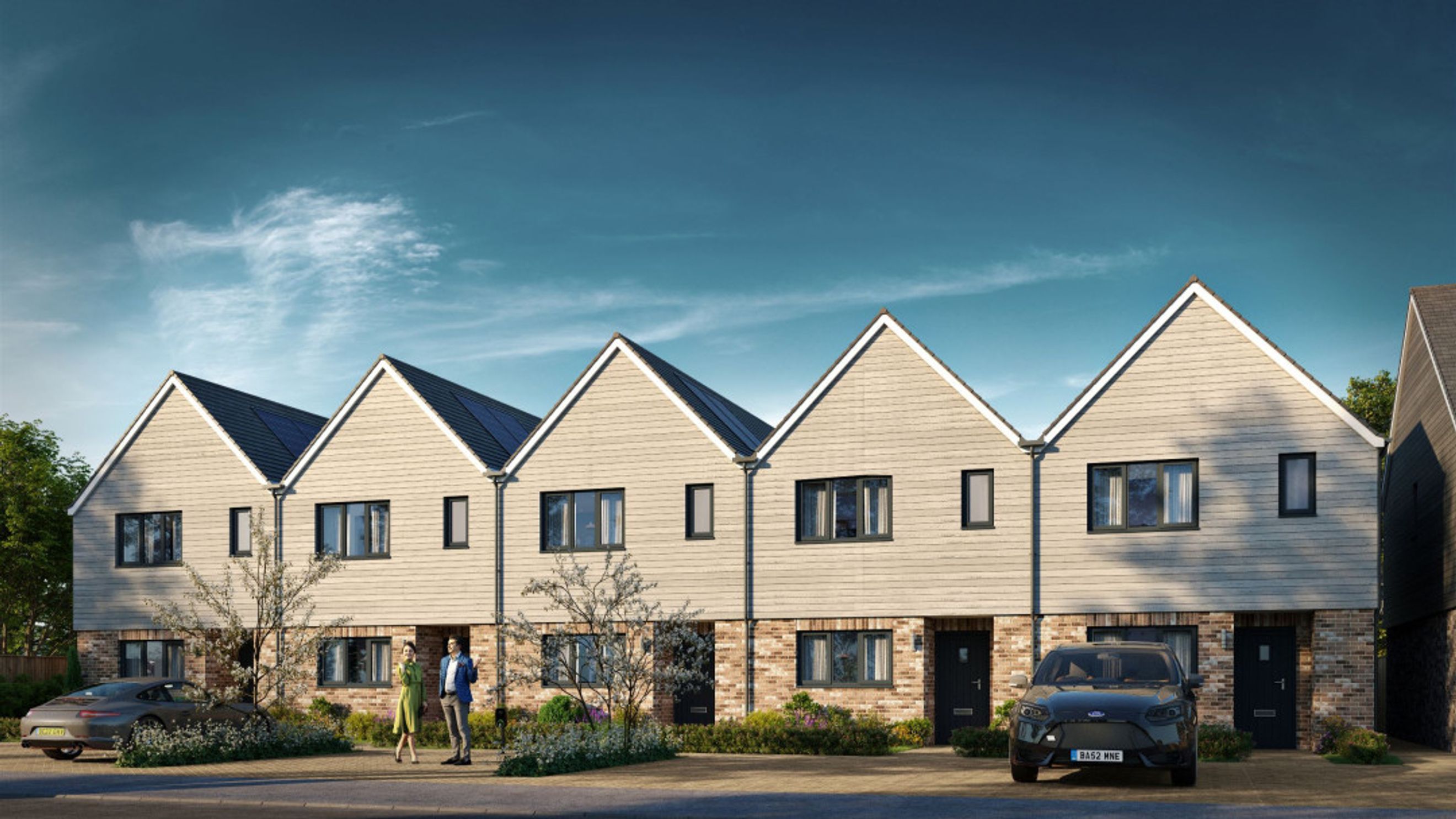 A row of modern townhouses with brick and timber facades, solar panels on the roofs, and parked cars in the driveways.
