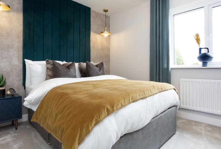A bedroom with a bed, pillows, a throw blanket, a bedside table, and a window.