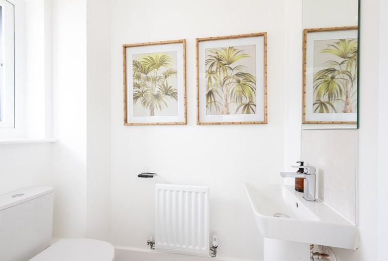 A bathroom with a toilet, sink, radiator, and artwork.