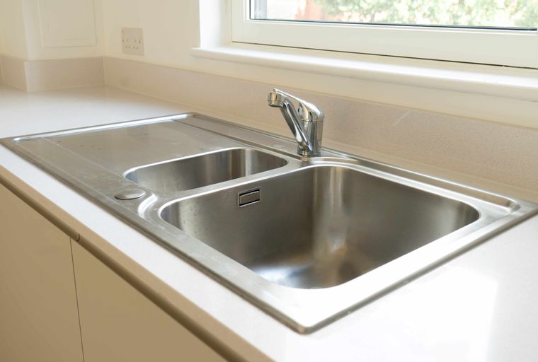 A double stainless steel sink with a chrome faucet is set into a light-colored countertop next to a window.