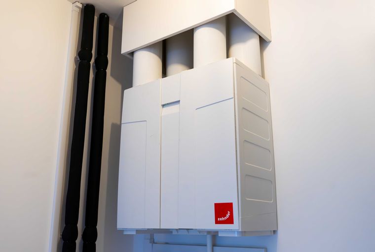 A white ventilation unit with black pipes mounted on a wall.