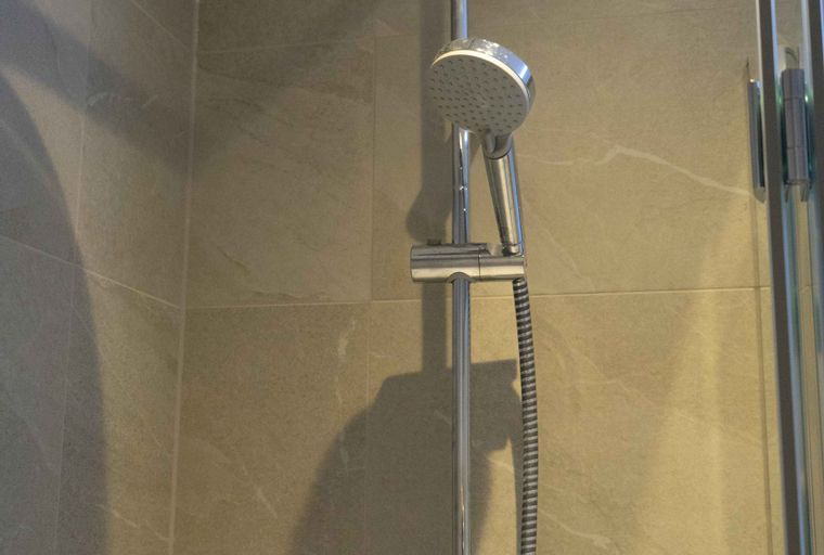 A showerhead system with a handheld attachment in a tiled shower stall.