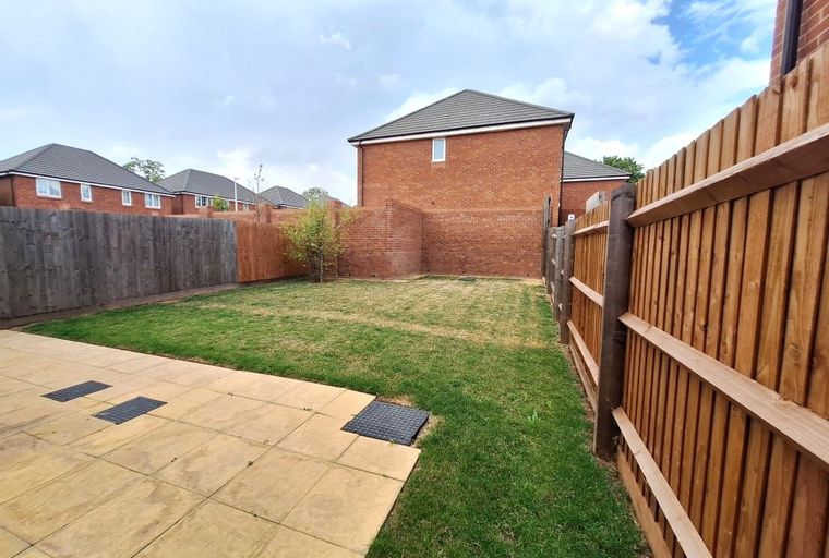 A backyard with a paved patio, a grassy lawn, and a wooden fence.