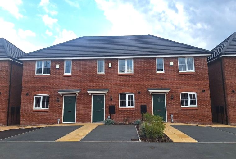 A row of new brick houses with dark roofs and green doors.