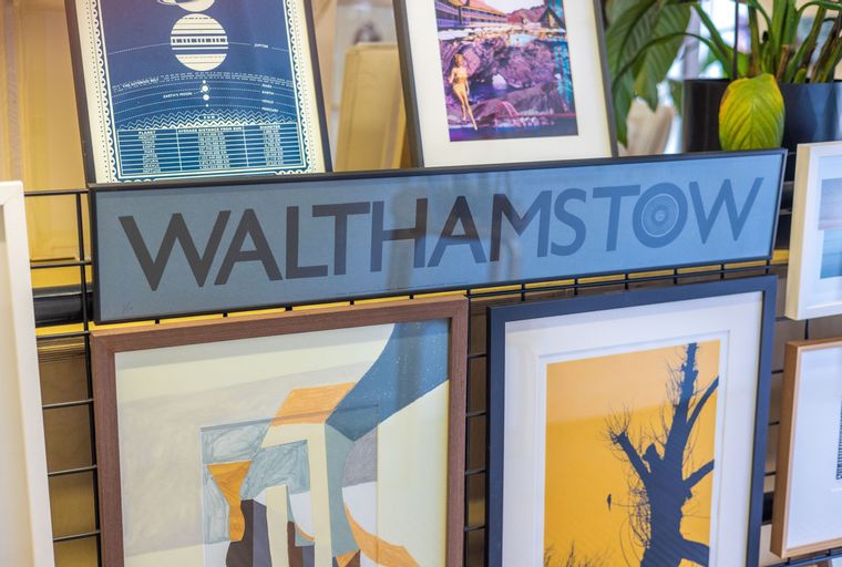 A sign that says 'WALTHAMSTOW' is displayed above several framed artworks.