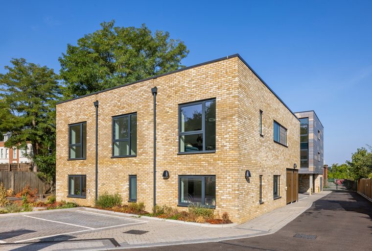 A modern yellow brick building with dark-framed windows and a paved driveway.