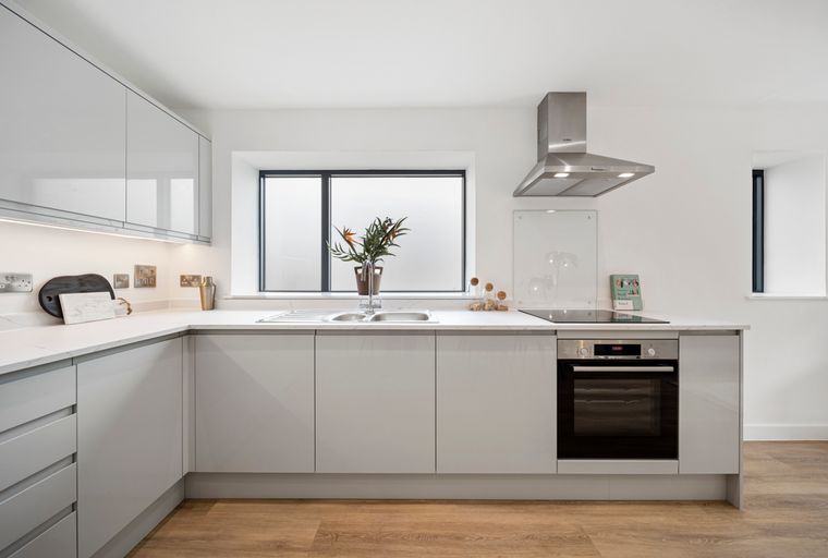 A modern kitchen with light grey cabinets, a quartz countertop, a double sink, and a built-in oven.