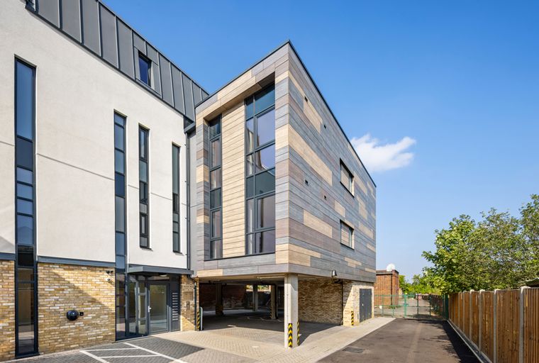 A modern building with a multi-textured facade and large windows, featuring covered parking underneath.