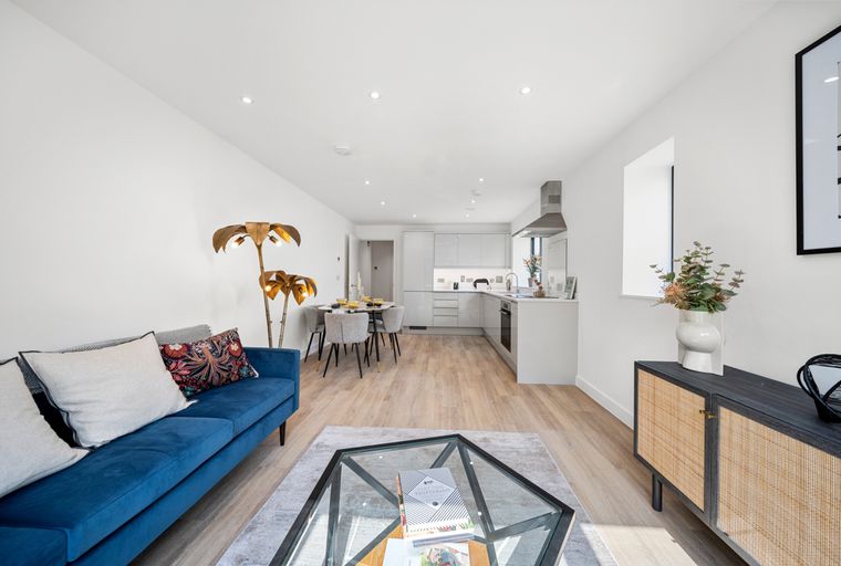 A living room and kitchen area with a blue sofa, dining table, and kitchen cabinets.