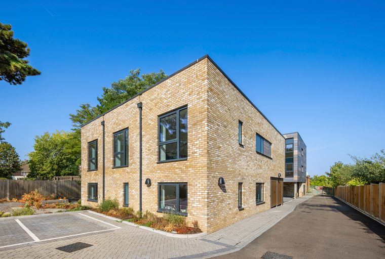 A modern yellow brick building with dark-framed windows and a paved driveway.