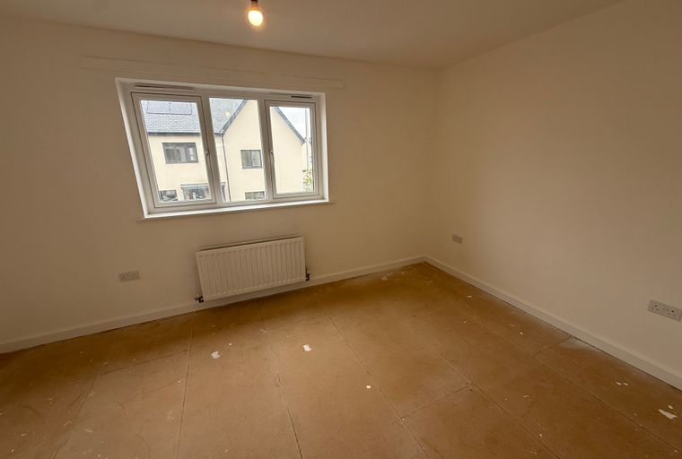A room with a window, radiator, and unfinished floor.
