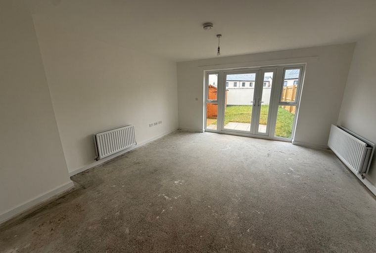 A living room with a concrete floor, double doors leading to a backyard, and two radiators.