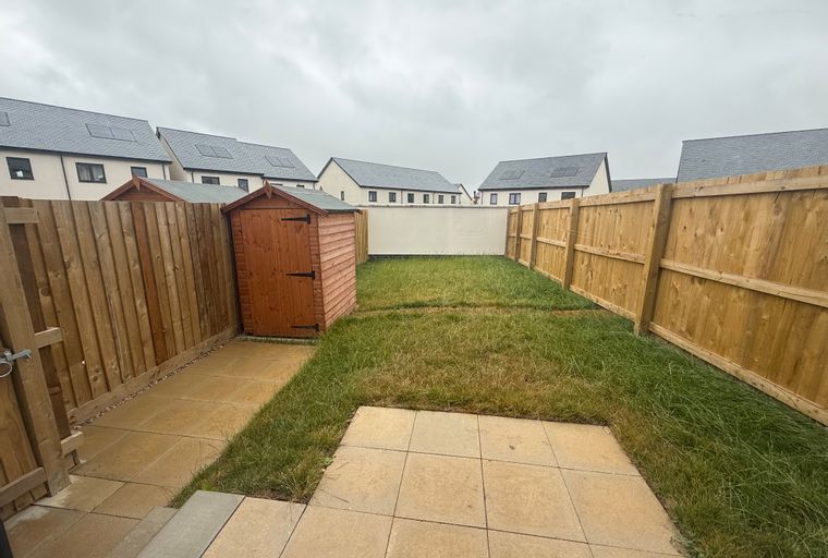 A backyard with a wooden shed, paved patio, and a wooden fence.