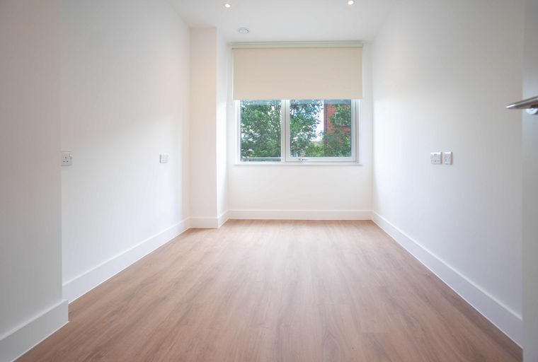 An empty room with a window and laminate flooring.
