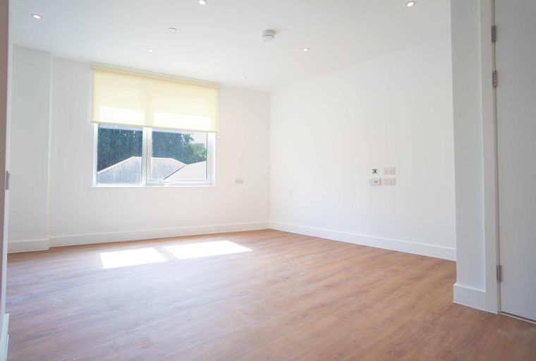 A spacious, unfurnished room with a window, laminate flooring, and electrical outlets.